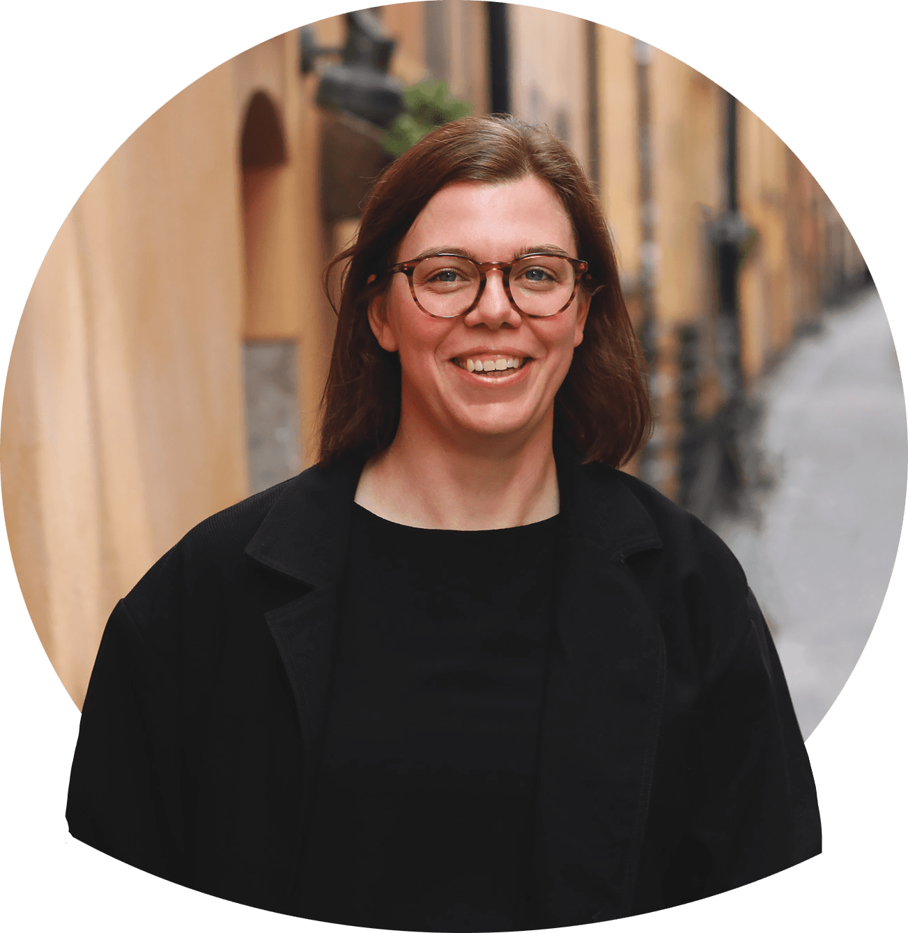 Frida S med briller og mørkt langt hår i jakke og topp, lener haken mot hånden. Foto.