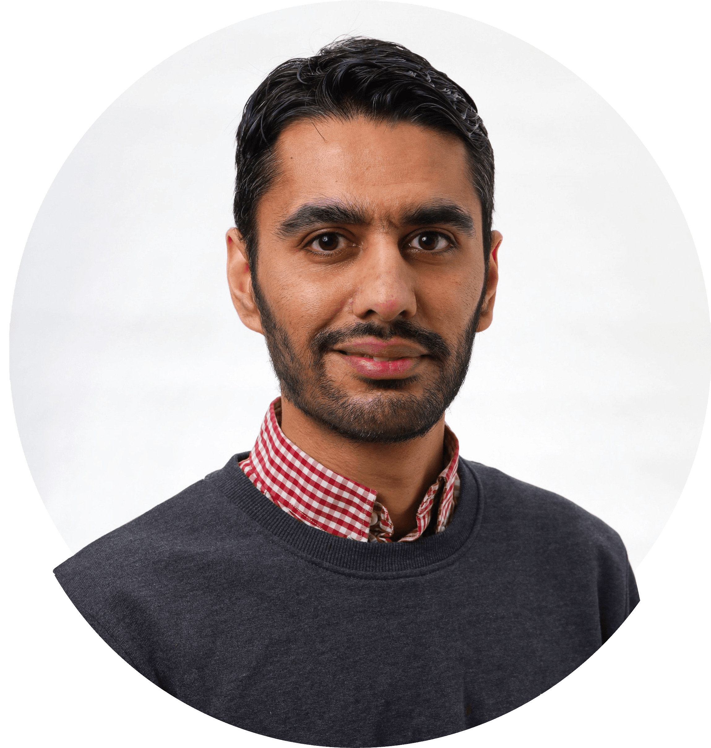 Danial smiler med mørkt hår og skjegg i rutete skjorte og mørk genser. Foto.