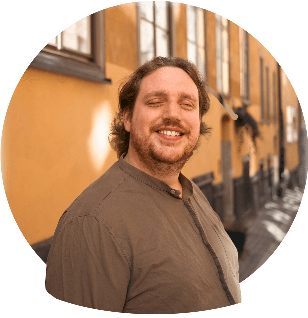 Christoffer er en mørkhåret mann med et stort smil, litt ansiktshår og en brun skjorte. Foto.