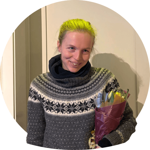 Amalie med lyst hår, iført grå mønstret genser, som holder en bukett blomster.